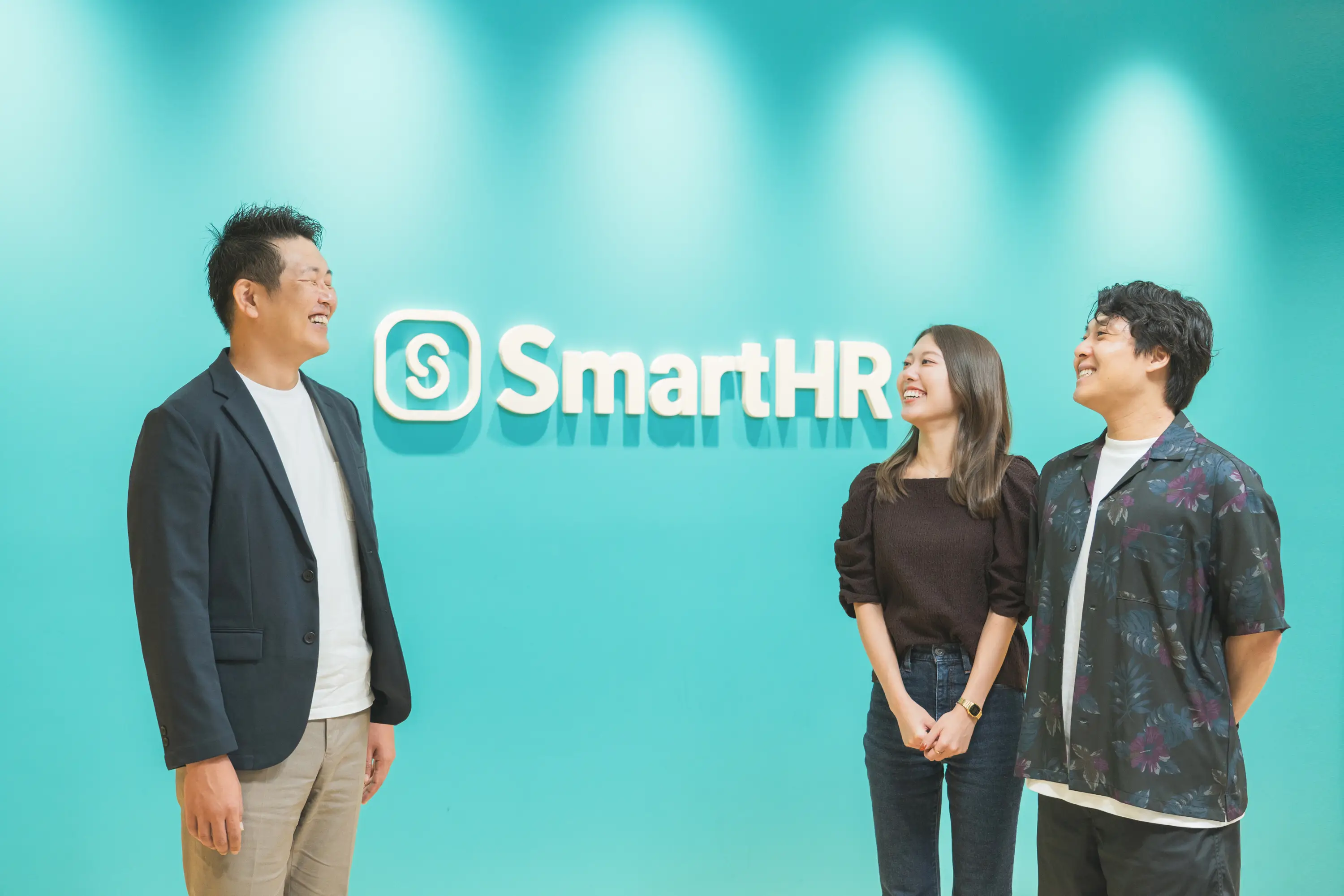 SmartHRさまのロゴの前で談笑するSells up代表の武田